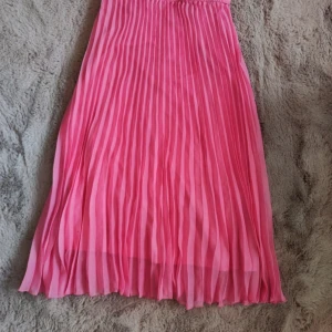 Rosa plisserad långkjol - Säljer en snygg rosa plisserad långkjol med elastisk midja. Kjolen har ett luftigt och flowy tyg som ger en fin siluett. Perfekt för dig som vill ha en färgklick i garderoben! Aldrig använd 