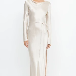 Champagnefärgad långklänning i satin - Elegant långklänning i skimrande champagnefärgad satin med lång ärm, slits och knytband i midjan. Klänningen har en vacker öppen rygg med knytning och en mjukt draperad halsringning. Perfekt för bal, brölopp eller andra festligheter. https://www.becandbridge.com/products/moon-dance-l-s-maxi-dress-sand