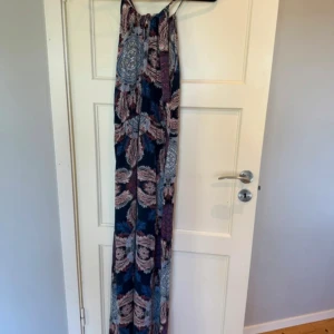 Mönstrad långklänning från Vero Moda - Lång klänning med ett vackert paisley-mönster i blått, lila och rosa toner. Klänningen har smala axelband och en avslappnad passform.