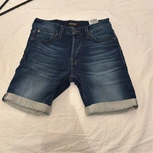 Jeansshorts från Jack & Jones - Mörkblå jeansshorts från Jack & Jones med klassisk femficksdesign och uppvikta benslut. Modellen är regular fit och har detaljerade sömmar på bakfickorna. Perfekta för varma dagar.