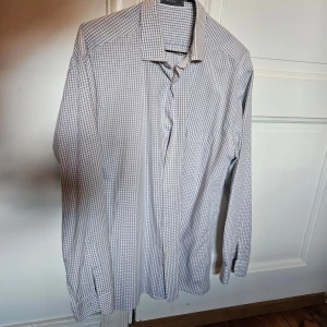 Rutig skjorta från Merxi - Klassisk långärmad skjorta från Merxi i vitt och grått rutigt mönster. Skjortan har knappar framtill och en klassisk krage. Perfekt för en stilren och avslappnad look.