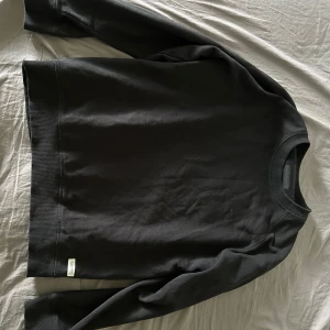 Svart sweatshirt från 157 - En enkel svart sweatshirt från 157 i storlek M. Tröjan har rund halsringning och långa ärmar, perfekt för en avslappnad stil. Tillverkad i mjukt material som känns skönt mot huden.