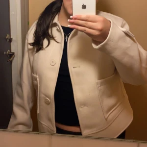 Beige kort jacka storlek M funkar S oxå  - Säljer en beige kavaj med stora fickor och knappar framtill. Jackan har en rak passform och är långärmad. Perfekt för dig som vill ha en stilren och enkel look.