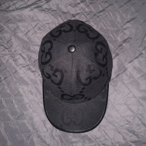 Svart Gucci Jumbo Keps - Säljer en svart keps från Gucci med tydligt GG-monogram i mörkgrått. Kepsen har böjd skärm och justerbar rem baktill. Snygg och stilren accessoar med exklusiv känsla och diskret mönster. Helt ny.