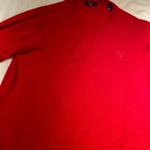 Röd stickad tröja från GANT - Säljer en klassisk röd stickad tröja från GANT i storlek M. Tröjan har rund halsringning och diskret broderad logga på bröstet. Perfekt för dig som gillar stilrena och tidlösa plagg.