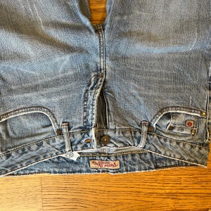 Blå jeans från Paris Blues med bootcut - Säljer ett par klassiska blå jeans från Paris Blues med bootcut och normal passform. Jeansen har fem fickor, knappgylf och snygga detaljer på bakfickorna. Perfekta för dig som gillar en tidlös denimlook.