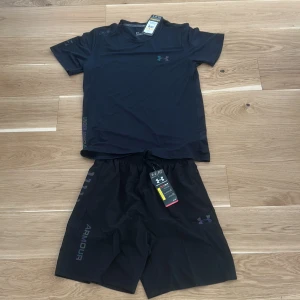 Svart t-shirt från Under Armour - Svart t-shirt från Under Armour med diskret logga på bröstet. T-shirten har rund halsringning och är tillverkad i ett lätt och funktionellt material som passar perfekt för träning, men även ute i vardagen. Denna sprillans nya under armour tracksuiten är helsvart och har jätteskönt lätt material. Pris kan diskuteras privat.