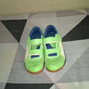 Gröna sneakers med kardborre från Puma - Säljer ett par gröna sneakers från Puma med vita och blå detaljer. Skorna har två breda kardborreband och en klassisk gummisula. Perfekta för dig som gillar färg och sportig stil!