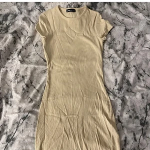 Beige ribbad klänning från FB Sister - Säljer en beige ribbad kortärmad klänning från FB Sister i storlek M. Klänningen har en tight passform och rund halsringning. Perfekt för dig som gillar enkel och stilren design.