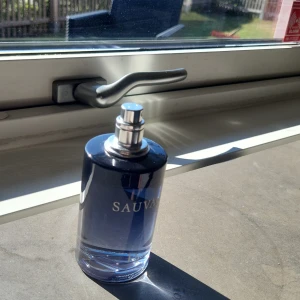 Sauvage parfym från Dior - En stilren parfymflaska från Dior Sauvage med mörkblå glas och silverfärgad spraykork. Flaskan har en rund form och tydlig logga framtill. Perfekt för dig som gillar fräscha och maskulina dofter. Parfymen är typ helt full.