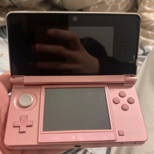 Rosa Nintendo 3DS med laddare och stylus - Säljer en rosa Nintendo 3DS med tillhörande laddare och stylus. Konsolen har dubbla skärmar, inbyggda kameror och klassiska Nintendo-knappar. Perfekt för portabelt spelande och retrospel. Färg: ljusrosa. Svår att hitta med detta pris och skick