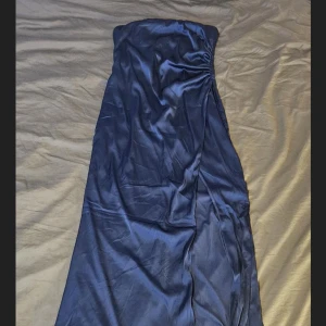 Marinblå axelbandslös långklänning i satin - Säljer en marinblå axelbandslös långklänning i glansigt satinmaterial. Klänningen har en elegant och enkel design med lätt drapering upptill. Perfekt för speciella tillfällen!