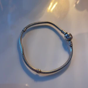 Silverarmband från Pandora - Säljer ett klassiskt silverarmband från Pandora med den ikoniska runda låset där Pandora-loggan är ingraverad. Perfekt för att samla och bära dina favoritberlocker. Stilren och tidlös design som passar till många tillfällen.