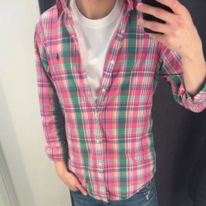 Ralph Lauren skjorta - Säljer en färgglad rutig skjorta från Ralph Lauren i storlek S. Skjortan har knappar framtill och klassisk krage. Färgerna är rosa, grön och vit. Perfekt för dig som vill ha en unik stil.