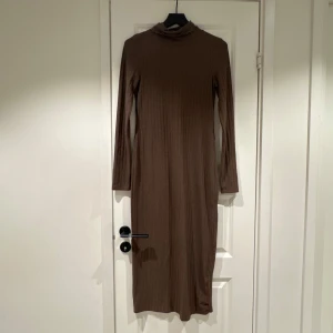 Brun ribbad långklänning från Bik Bok - Säljer en brun ribbad långklänning från Bik Bok med lång ärm och liten volangkant vid halsen. Klänningen har en figurnära passform och är perfekt för dig som gillar en enkel men stilren look. Storlek XS