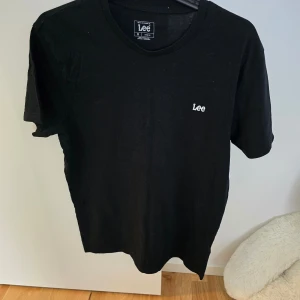 Svart t-shirt från Lee - Säljer en svart t-shirt från Lee med liten vit broderad logga på bröstet. Klassisk passform och rund halsringning. Tillverkad i 100% bomull, perfekt för en enkel och stilren look.