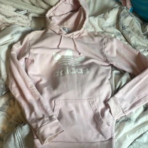 Ljusrosa hoodie från Adidas - Säljer en ljusrosa hoodie från Adidas med vit logga framtill. Tröjan har huva med dragsko och en stor magficka. Köpt i adidas butiken. Nypris runt 600-700. 