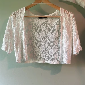 Vit spets bolero - Säljer en söt vit bolerotopp från Vila. Något sliten i armarna men inget man lägger märket till, men annars jättegulligt! St S-M