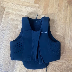 Säkerhetsväst från Komperdell - Säljer en svart skyddsväst från Komperdell Cross Protection. Västen har perforerade paneler för ventilation och dragkedja framtill. Perfekt för dig som vill ha extra skydd vid ridning. Snygg och sportig design med diskret logga på bröstet. Nypris 3799kr, säljs för 1950kr. Passa på!