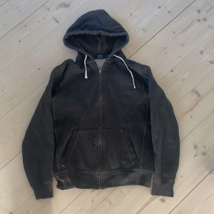 Mörkgrå hoodie från Polo Ralph Lauren - Säljer en mörkgrå hoodie från Polo Ralph Lauren med dragkedja och vit dragsko i huvan. Tröjan har en broderad röd logga på bröstet och två fickor framtill. Skick 6,5/10 därför har jag valt det här priset.