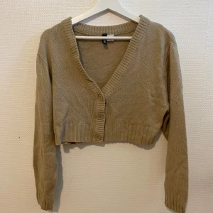 Beige kofta - Säljer en beige kofta från H&M med v-ringning och knappar framtill. Tröjan är stickad och har långa ärmar samt ribbade muddar. Perfekt för lager-på-lager-stil!