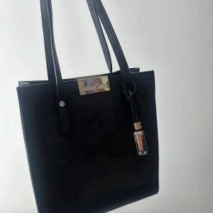 Svart axelväska och handväska från Michael Kors - Två stilrena Vintage svarta väskor från Michael Kors. Ena är en klassisk handväska med silverdetaljer och flätad remdetalj, den andra en smidig axelväska med justerbar rem och metallogo framtill. Materialet är mocka