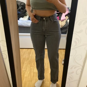 Gråa högmidjade jeans - Säljer ett par gråa högmidjade jeans med klassisk femficksdesign och raka ben. Jeansen har knapp- och dragkedjestängning framtill och är i ett mjukt denimtyg. Perfekta för en avslappnad och stilren look.