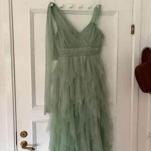 Ljusgrön balklänning med volanger från QR Fashion - Säljer en drömmig ljusgrön långklänning från QR Fashion med lager på lager av volanger i tunn tyll. Klänningen har v-ringad omlottringning. Perfekt för speciella tillfällen som bal. När jag köpte den stod det att den var i nyskick men när jag fick hem den såg jag att den var omsydd i överdelen med axelbanden, utöver det är den helt som ny. En aning stor i storleken, skulle nog säga S-M eller 38.