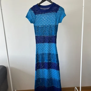 Blå stickad långklänning - Säljer en stickad långklänning i olika nyanser av blått med korta ärmar. Klänningen har ett genomgående hålmönster och är figurnära upptill. Perfekt för dig som gillar unika och färgstarka plagg!