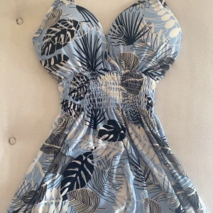 Blå sommarklänning med tropiskt mönster - Säljer nu två klänningar som är köpte i Grekland. Klänningen har smock i midjan, vadderad byst och smala axelband. Inläggen i bysten går att ta ut ifall man inte vill ha dem. Perfekt för varma dagar och har en luftig passform. 