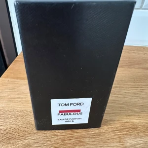 Tom Ford Fabulous Eau de Parfum 100 ml - Exklusiv parfym från Tom Ford i modellen Fabulous. Flaskan är matt svart med en stilren, fyrkantig design och vit etikett med svart och röd text. Innehåller 100 ml Eau de Parfum, perfekt för dig som gillar lyxiga och unika dofter.