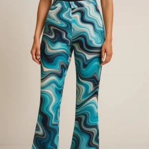 Blå mönstrade byxor med vågigt mönster - Säljer ett par riktigt snygga byxor med vågigt mönster i olika blå och turkosa nyanser. Byxorna har hög midja och utsvängda ben, perfekt för dig som vill sticka ut. Materialet känns mjukt och följsamt mot kroppen.