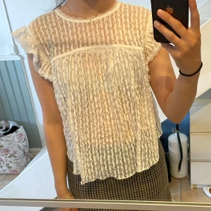 Vit&svart spetsblus med volangärm - Säljer en söt och luftig vit och svart blus i spets med korta volangärmar och rund halsringning. Blusen har ett fint mönster, är transparent och knyts i nacken. Är lite rundad ram och bak. Båda har kvar prislappen. Aldrig använda. 210 (st)