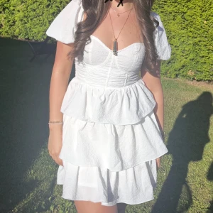 Vit volangklänning med puffärm - Säljer min studentklänning en söt vit klänning med volanger och puffärmar. Klänningen har en markerad midja och omlottkänsla upptill. Perfekt för sommarens alla tillfällen! 💫