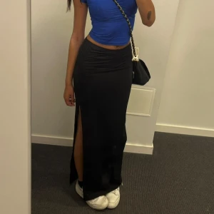 Svart långkjol med slits - Säljer en svart långkjol med hög slits på ena sidan. Kjolen har en tight passform och är perfekt att styla med sneakers eller klackar. Enkel och stilren design som passar till många olika looks.