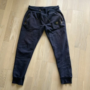 Mjukisbyxor från MR Originals  - Svarta mjukisbyxor med resår och snörning i midjan samt gulddetaljer på snörena. På vänster ben finns ett svart märke med en guldfärgad krona och texten 'MR'. Byxorna har muddar vid bensluten för en skön passform. Ny priset är runt 800 kr och är en mycket populär byxa.