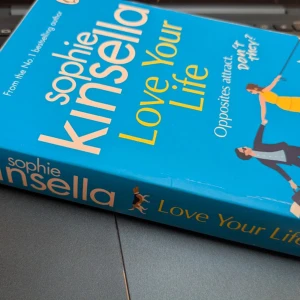 Love Your Life - En färgstark och charmig bok om oväntad kärlek och möten mellan olika personligheter. Perfekt för dig som gillar romantik, humor och feelgood. Omslaget utstrålar glädje och energi, vilket gör den till ett härligt tillskott i bokhyllan.