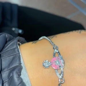Vivienne Westwood armband med rosa orb - Säljer ett armband från Vivienne Westwood med silverfärgad kedja och det klassiska orb-hänget i rosa och silver. Säljer då jag fick det av mitt ruttna ex, använder inte ens silver smycken. Det är nästan helt nytt, nypris är 1500:- jag säljer för 900:-