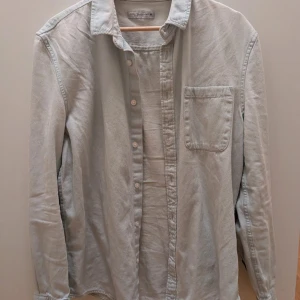 Ljusgrå jeansskjorta från Cedar Wood State - Säljer en ljusgrå jeansskjorta från Cedar Wood State i storlek M. Skjortan har klassisk krage, bröstficka och knäppning framtill. Perfekt att bära öppen eller stängd för en avslappnad stil.