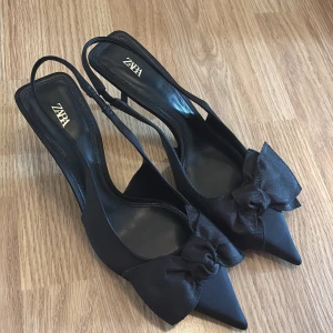 Svarta pumps med rosett från Zara - Säljer ett par oanvända svarta klackskor storlek 39 från Zara. Skorna har rosetter smal klack. Slutsålda i butik