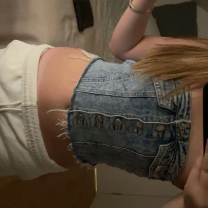 Jeans tubtopp med knappar - Säljer en jättefin croppad jeans tubtopp i ljusblå denim med knappar framtill och råa kanter. Den har en tight passform och smockad baksida för extra komfort. Super fin och har använt 1 gång innan 💗