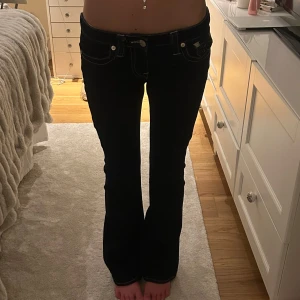Mörkblå bootcut jeans från True Religion - Säljer ett par mörkblå jeans från True Religion, modell BECCA Mid Rise Bootcut. Jeansen har vita kontrastsömmar, klassiska fickor bak och bootcut passform. Perfekta för dig som gillar en tidlös jeansstil.