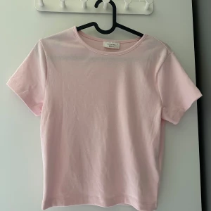 Ljusrosa t-shirt från Gina Tricot - Säljer en ljusrosa t-shirt från Gina Tricot, basically basics-kollektionen. T-shirten har rund halsringning och korta ärmar. Enkel och stilren modell i mjuk bomull, perfekt för en avslappnad look.