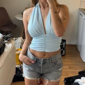 Ljusblå halterneck topp med knyt - Säljer en ljusblå halterneck topp med knyt i nacken och rynkade detaljer framtill. Toppen är använd 2 gånger och i topp skick. 