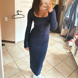 Marinblå långärmad långklänning - Säljer en marinblå långklänning med lång ärm och snygg rynkad detalj längs sidorna. Klänningen har en fyrkantig urringning och är figurnära med stretchigt material som sitter riktigt snyggt. 