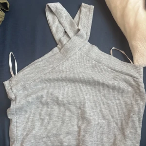 Ljusgrå ribbad linnetopp - Supersnygg ljusgrå ribbad linnetopp med breda korsade axelband. Toppen är ärmlös och har en tight passform som framhäver siluetten. 