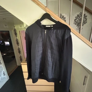 Cardigan ifrån kappahl - Svart hoodiejacka från Morris med quiltad front och mjuka ärmar. Jackan har huva, hel dragkedja och ribbade muddar. Perfekt för lager-på-lager och chill vardagsstil.