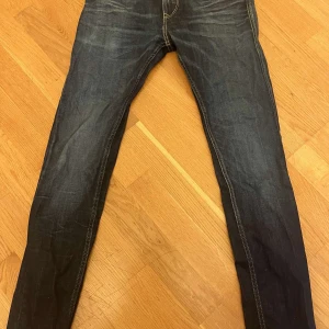 Replay jeans i mörkblå denim, stl 30 - Säljer ett par snygga Replay jeans i mörkblå tvätt med klassiska kontrastsömmar och coola bakfickor. Jeansen har smal passform och är tillverkade i slitstark denim. Perfekta för dig som gillar en stilren och modern look.