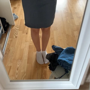 Mörkgrå kort kjol med slits - Enkel och stilren mörkgrå kort kjol i mjuk mix av polyester och bomull med lite stretch. Modellen är rak och har en liten slits på ena sidan för en snygg detalj. Den är använd ett antal gånger, men har inga fläckar eller slitage som jag hittar. Den är normal i storleken men ha ett resårband som går att töjas. 