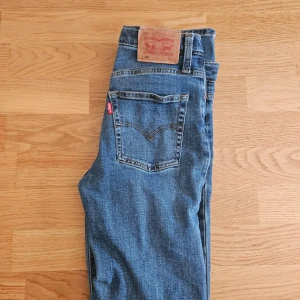 Levi's 501 blå jeans 152 cm - Klassiska blå Levi's 501 jeans i rak modell med fem fickor och knappgylf. Snyggt mellanblå tvätt och ikonisk läderpatch bak i midjan. Perfekta för dig som gillar tidlös denimstil och vill ha ett par jeans som alltid funkar.